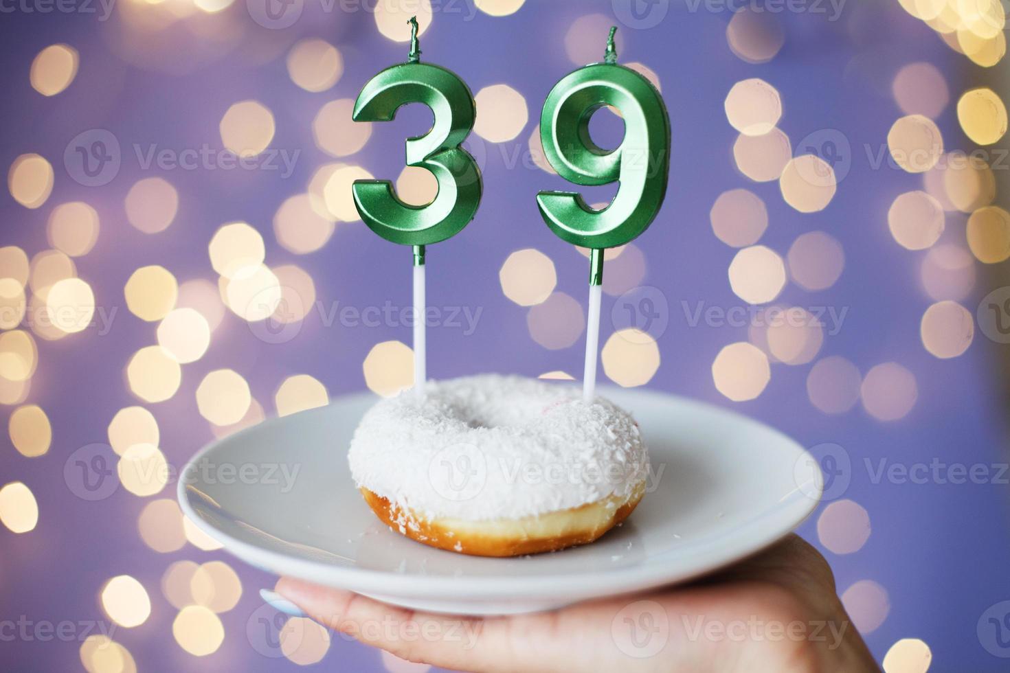 woman holding a cake with the number 39 candles on festive blurred bokeh background photo