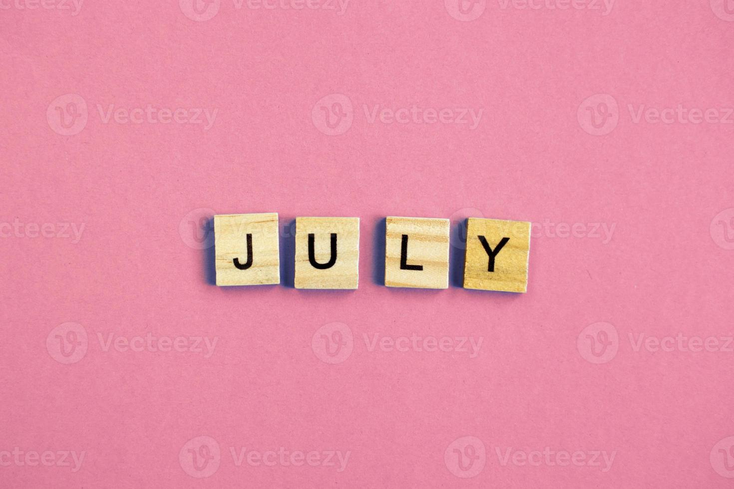 inscription July made by wooden cubes on a pastel pink background. photo