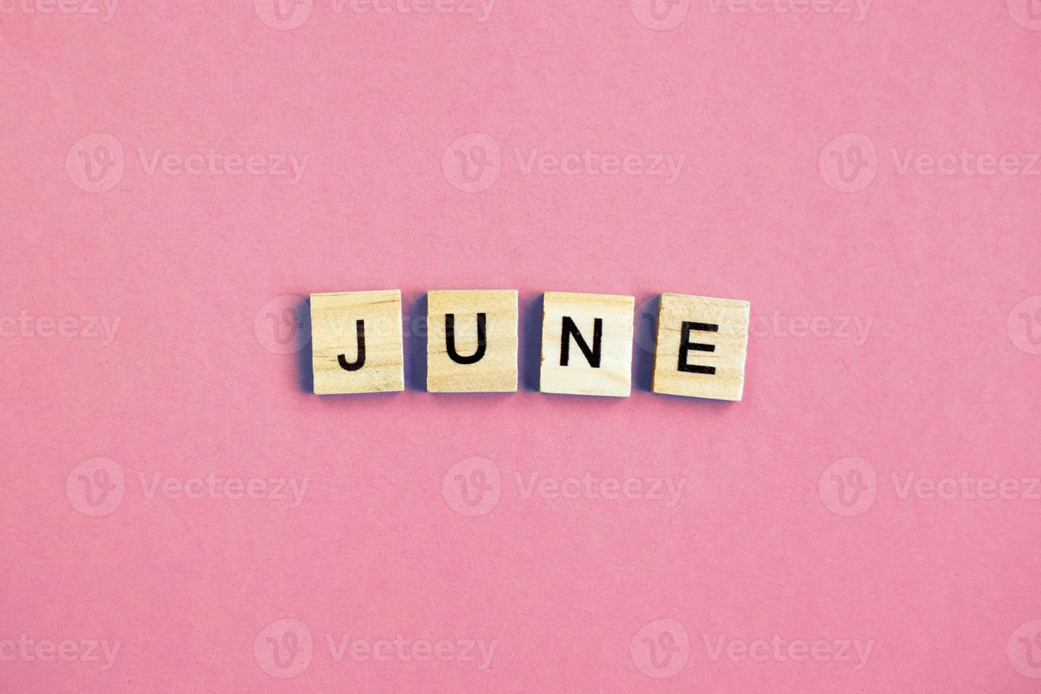 inscription June made by wooden cubes on a pastel pink background. photo