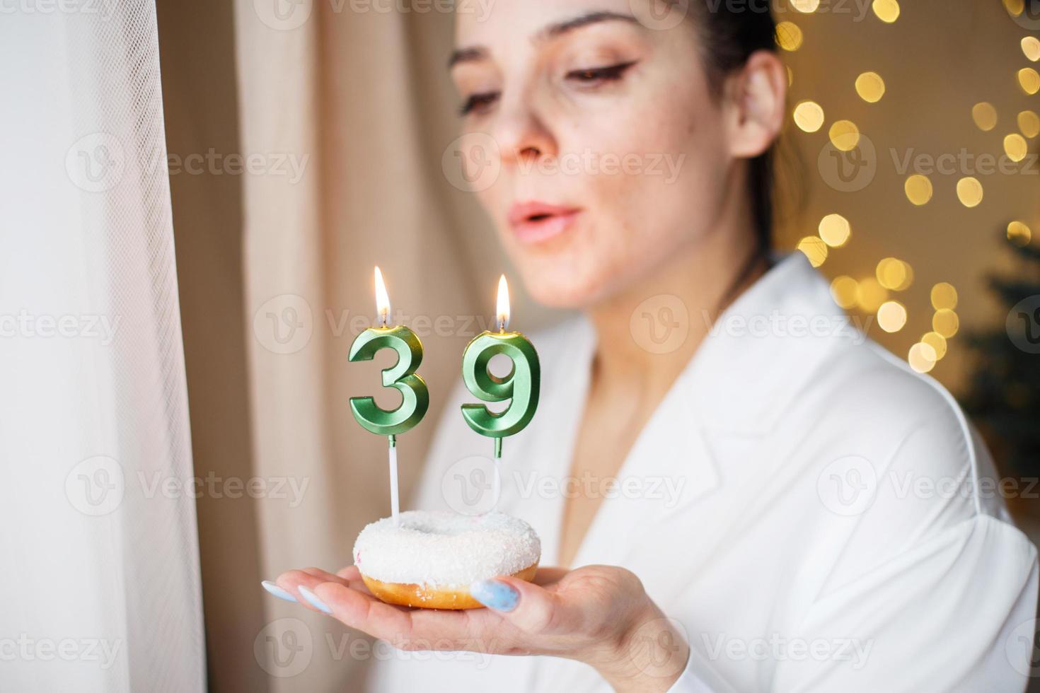 woman holding a cake with the number 39 candles on festive blurred bokeh background photo