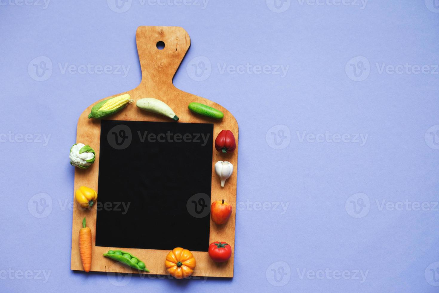 vegetables and fruits on the cutting board on purple background. healthy cooking concept photo