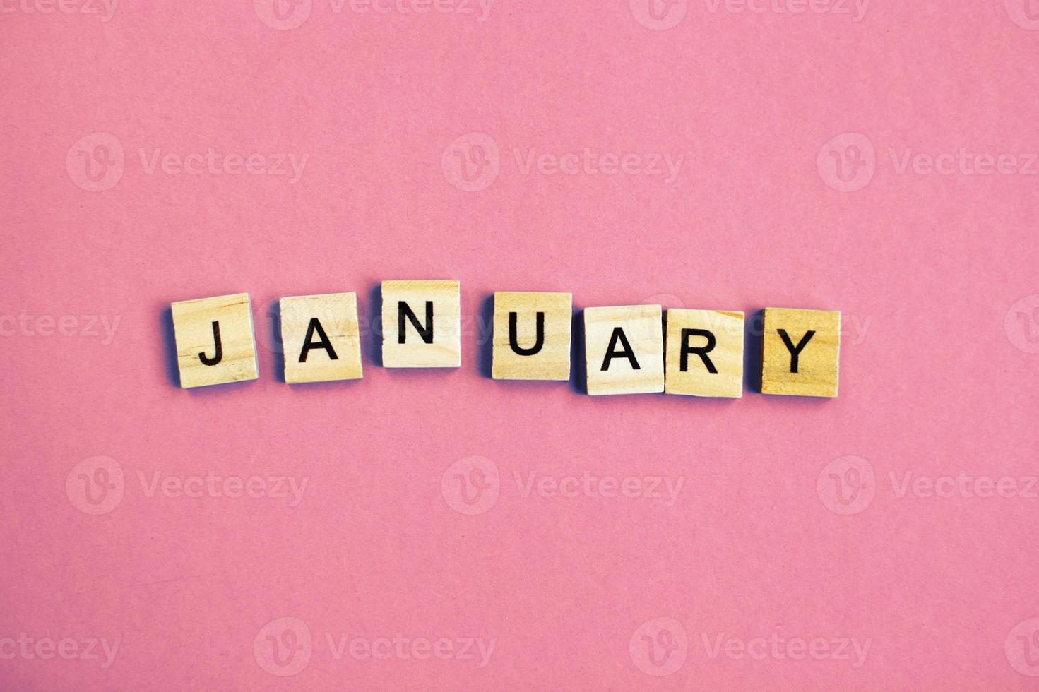inscription January made by wooden cubes on a pastel pink background. photo