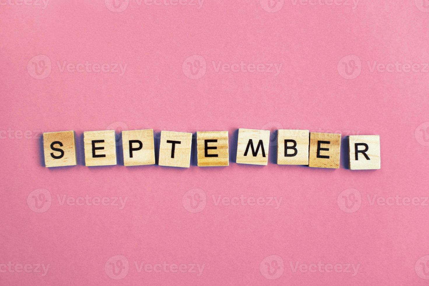 inscription September made by wooden cubes on a pastel pink background. photo