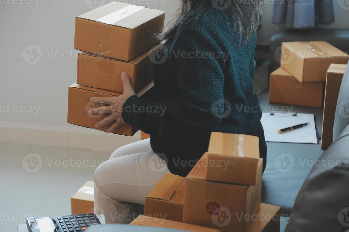 Startup SME small business entrepreneur of freelance Asian woman wearing apron using laptop and box to receive and review orders online to prepare to pack sell to customers, online sme business ideas. photo