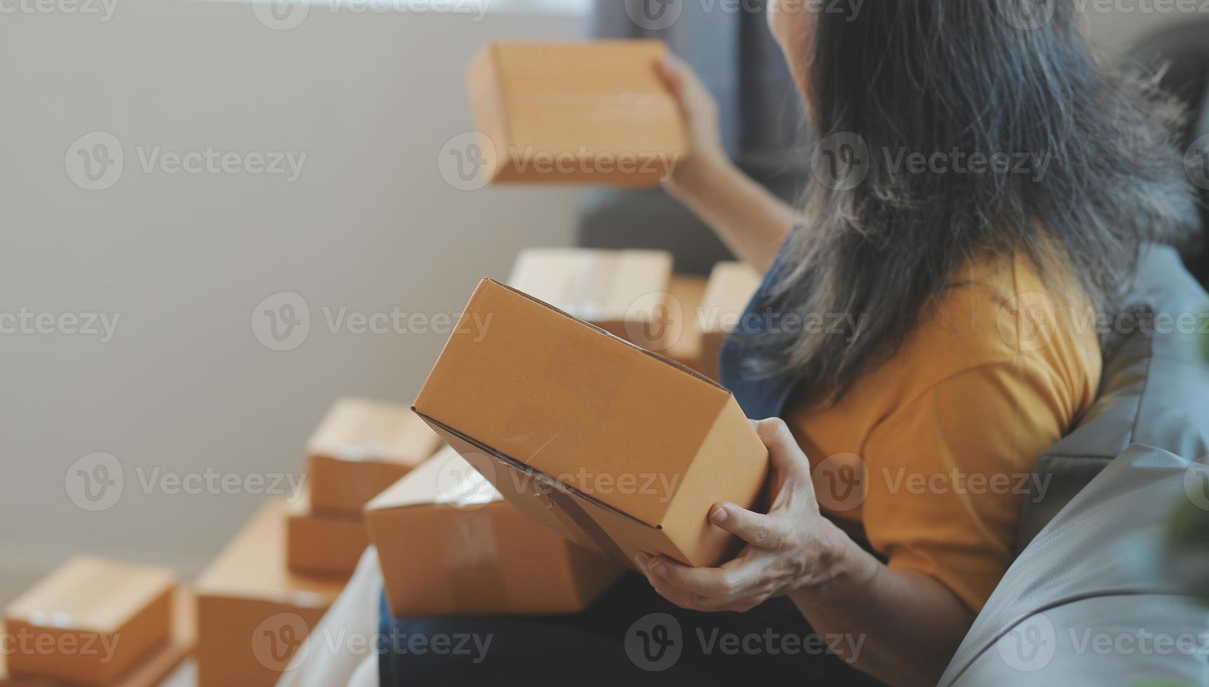 Startup SME small business entrepreneur of freelance Asian woman wearing apron using laptop and box to receive and review orders online to prepare to pack sell to customers, online sme business ideas. photo