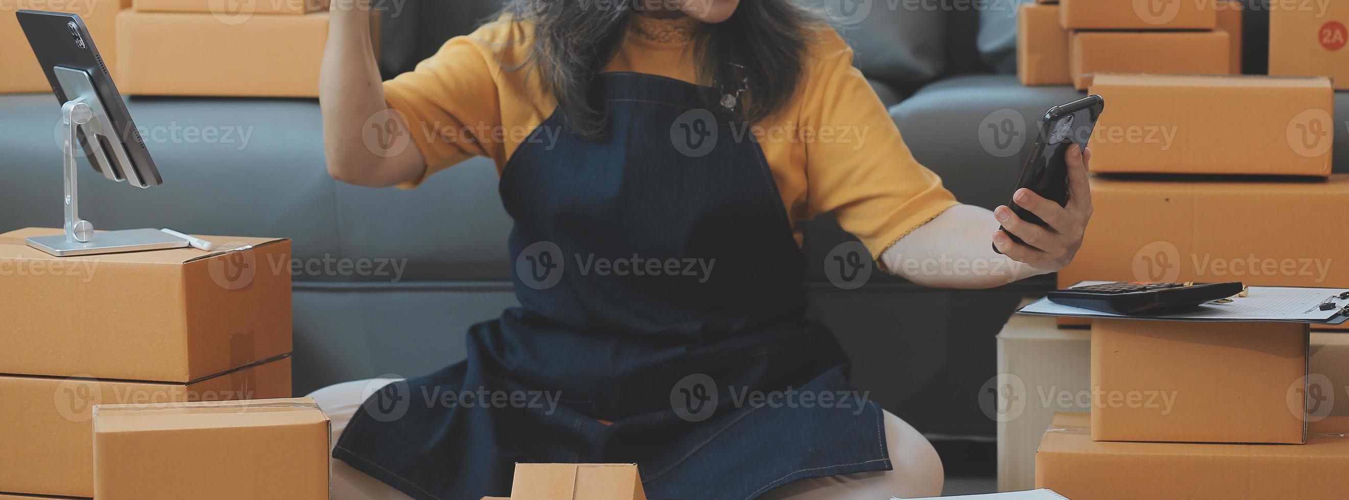 Startup SME small business entrepreneur of freelance Asian woman wearing apron using laptop and box to receive and review orders online to prepare to pack sell to customers, online sme business ideas. photo