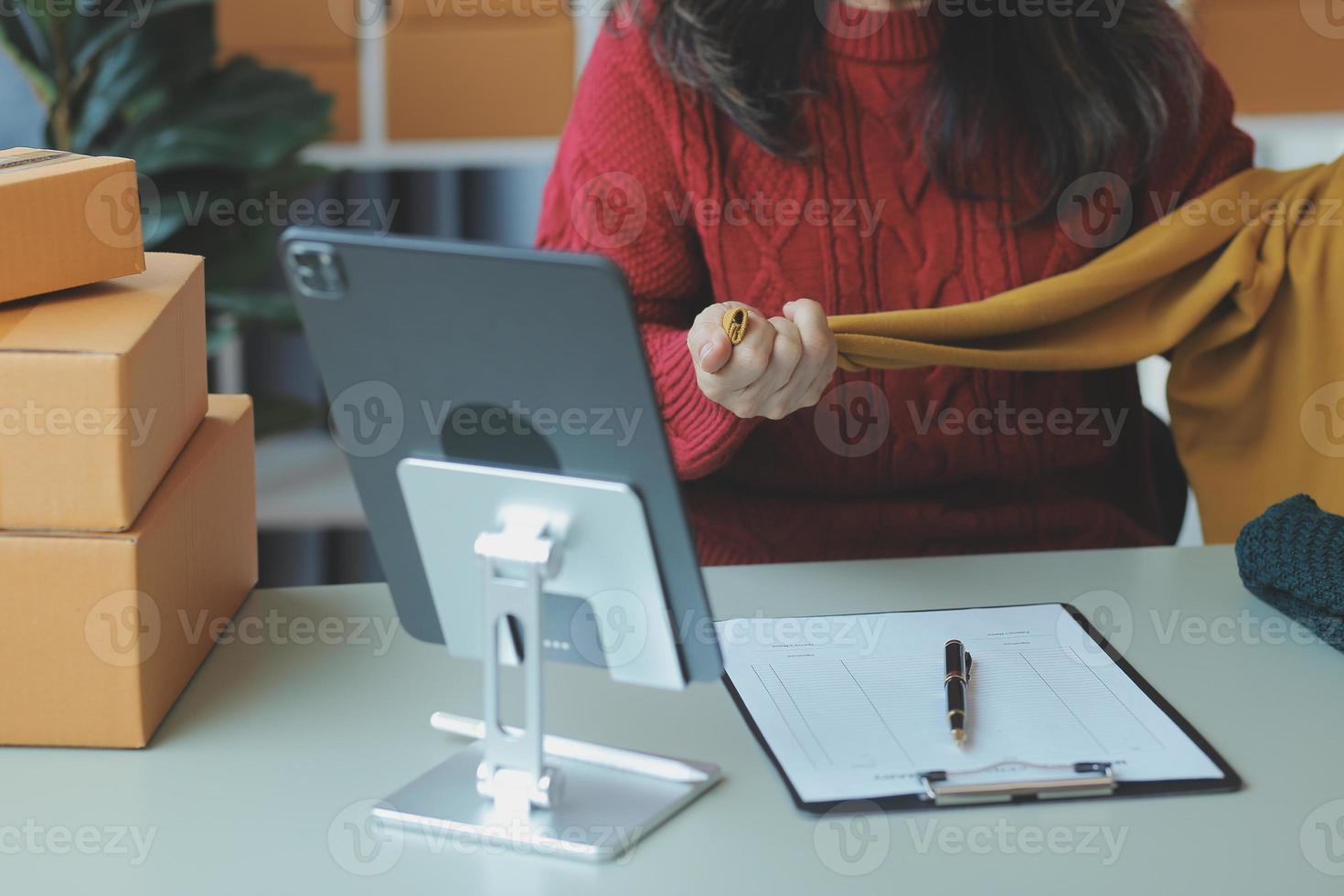 Startup SME small business entrepreneur of freelance Asian woman wearing apron using laptop and box to receive and review orders online to prepare to pack sell to customers, online sme business ideas. photo