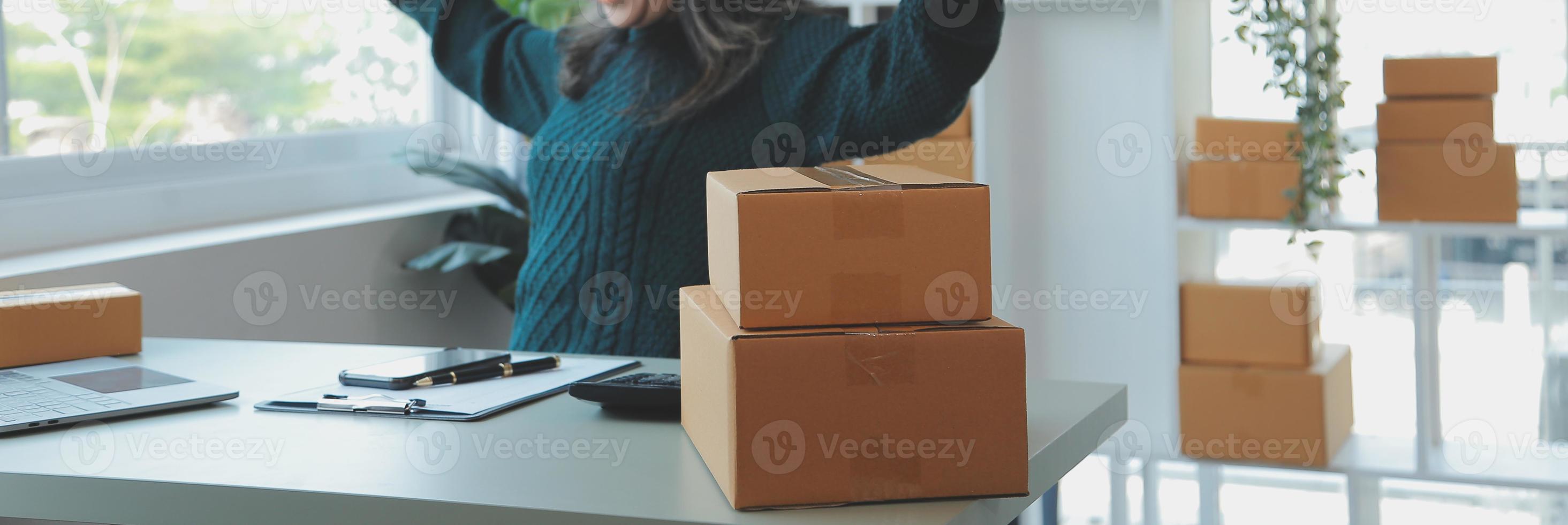 Startup SME small business entrepreneur of freelance Asian woman wearing apron using laptop and box to receive and review orders online to prepare to pack sell to customers, online sme business ideas. photo