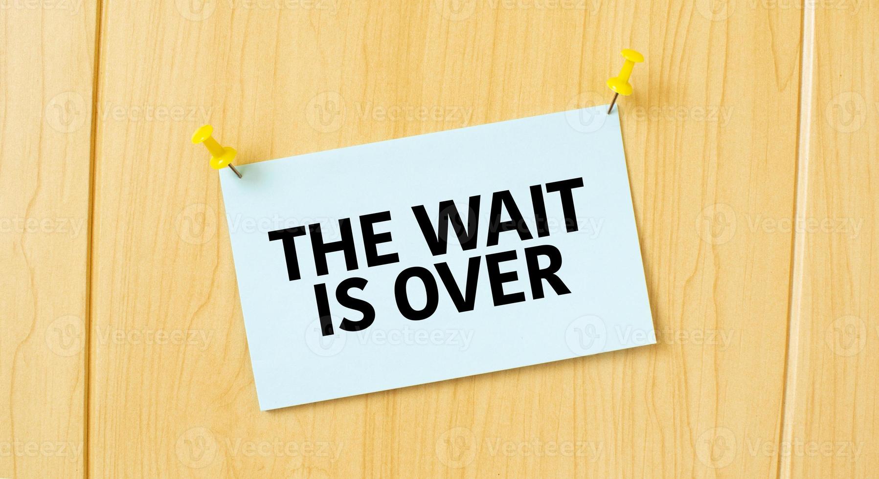 the wait is over sign written on sticky note pinned on wooden wall photo