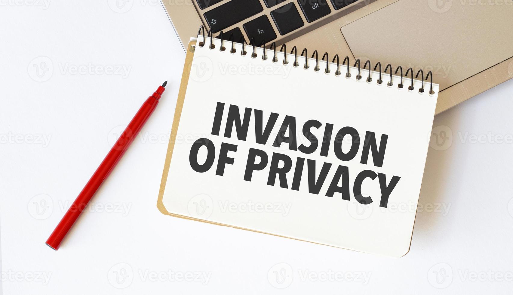 Laptop, red pen and notepad with text invasion of privacy in the white background photo