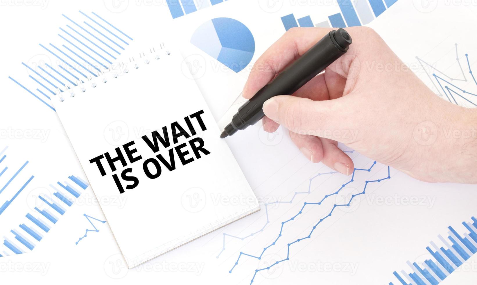 Businessman holding a black marker, notepad with text the wait is over , business concept photo