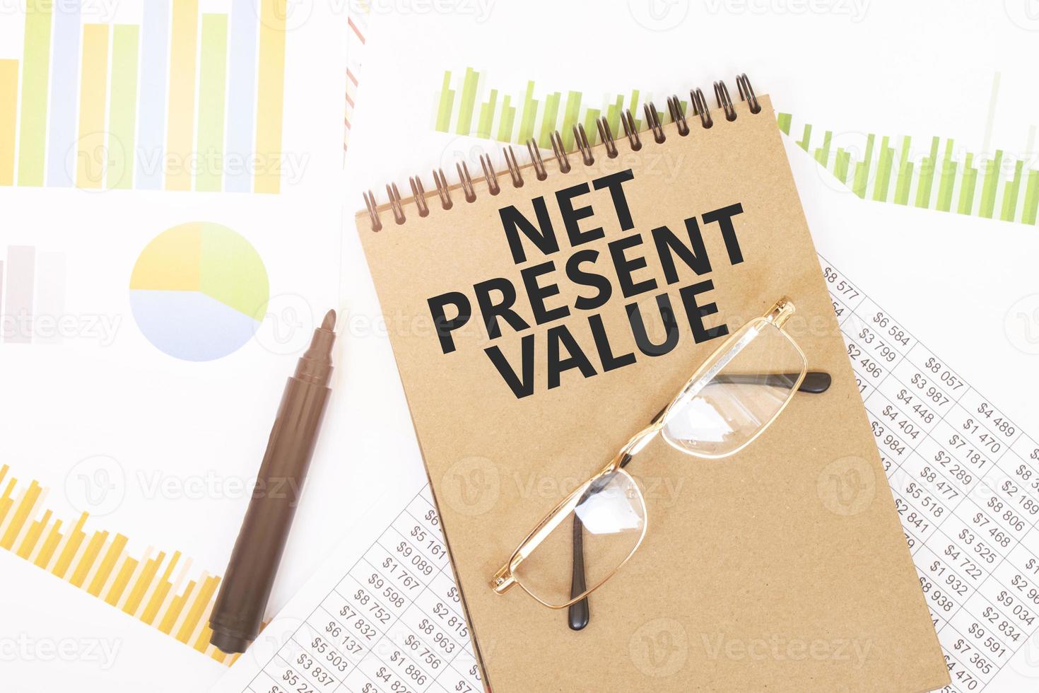 In a craft colour notebook is a net present value inscription, next to pencils, glasses, graphs and diagrams. photo