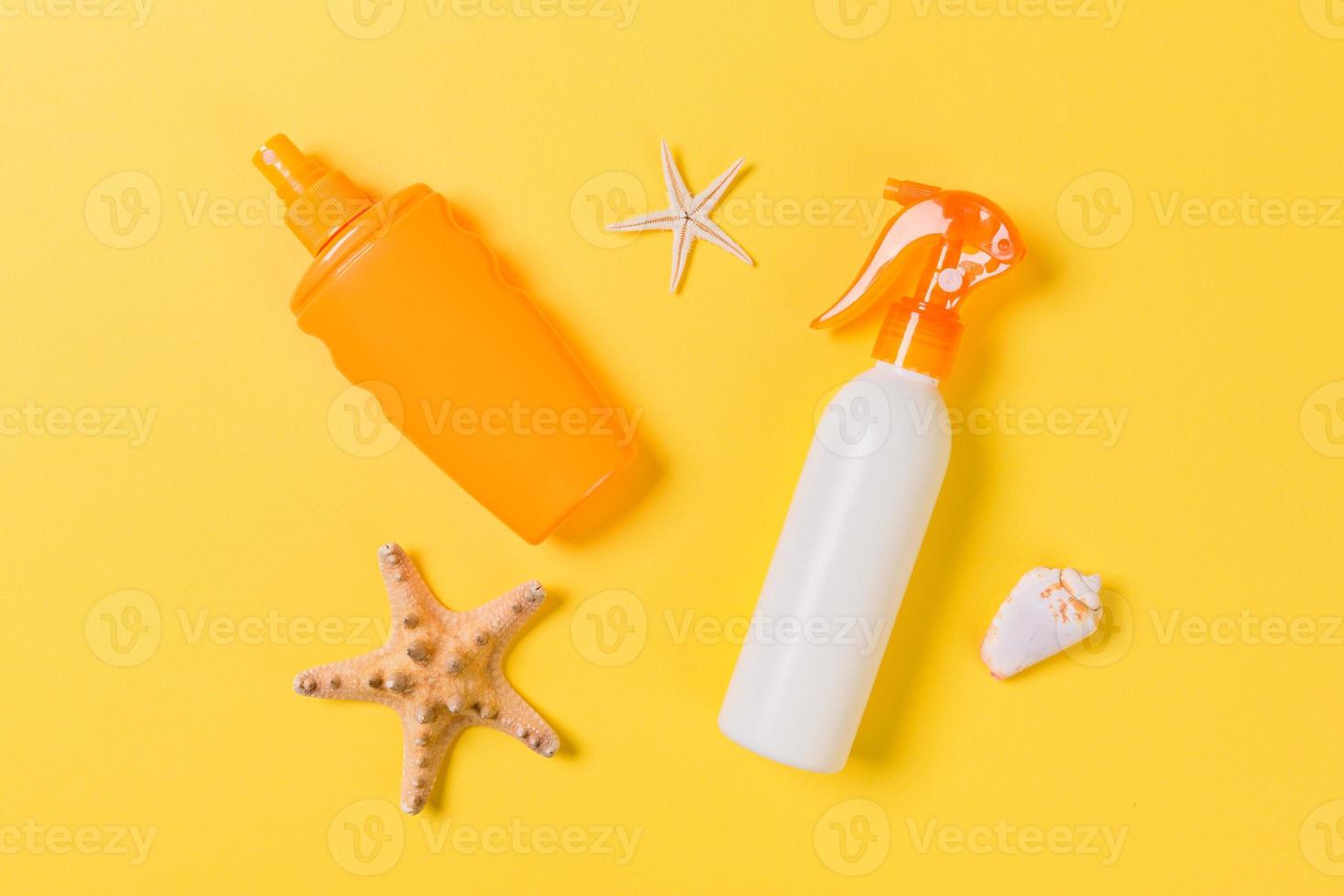 sunscreen cream with starfish and seashells in bottles on yellow background, top view photo