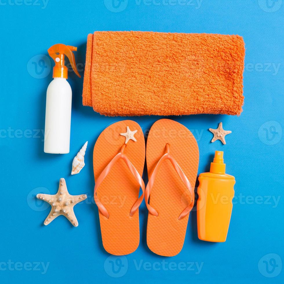 Top view of Beach flat lay accessories. sunscreen bottle with seashells, starfish, towel and flip-flop on Colored background with copy space photo