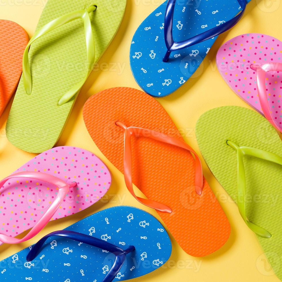 many colored flip flops on yellow background. Copy space top view photo