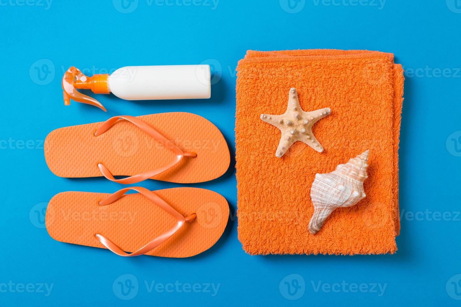 Top view of Beach flat lay accessories. sunscreen bottle with seashells, starfish, towel and flip-flop on Colored background with copy space photo
