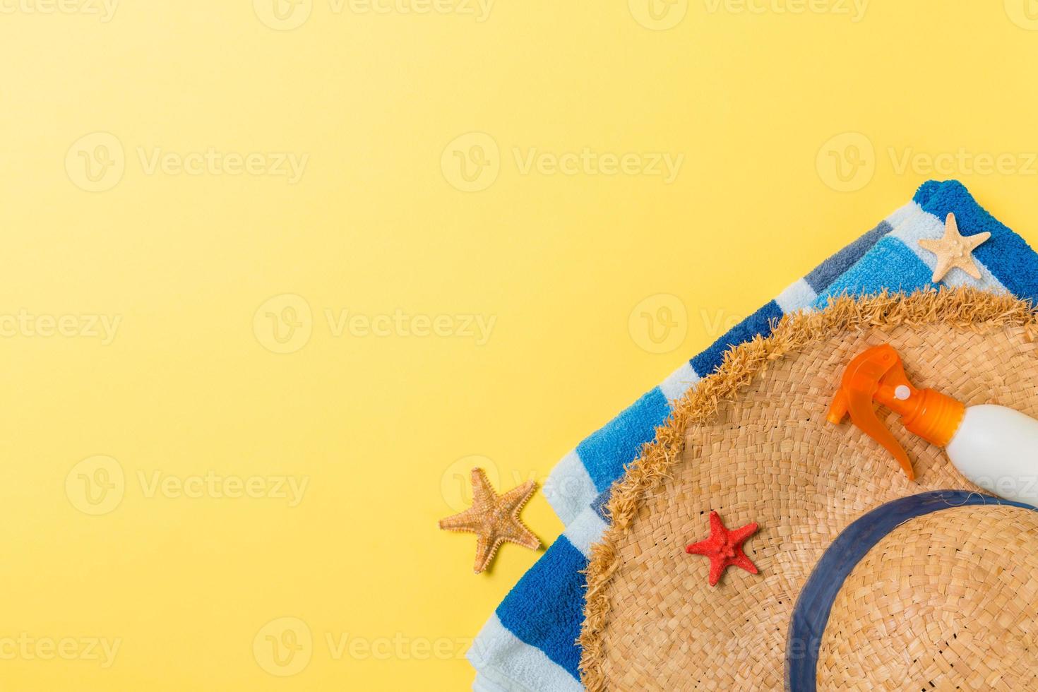Beach flat lay accessories with copy space. Striped blue and white towel, seashells, staw sunhat and a bottle of sunblock on yellow background. Summer holiday concept photo