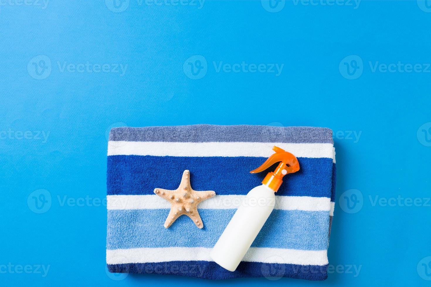 Summer beach flat lay accessories. Sunscreen bottle cream, towel and seashells on colored Background. Travel holiday concept with copy space photo