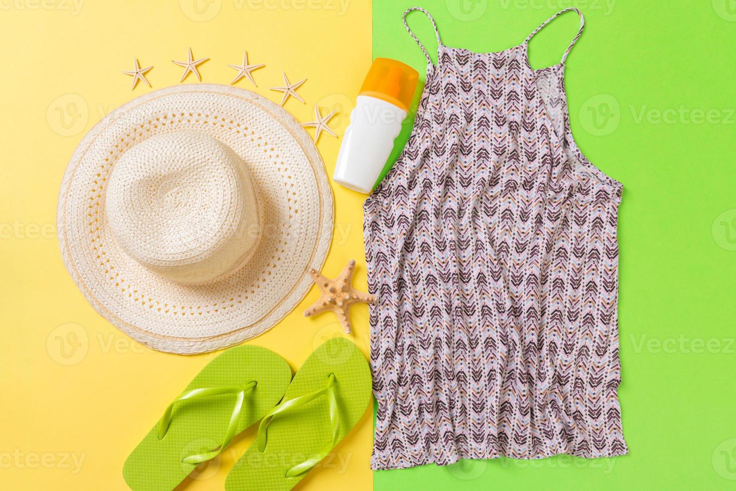 Summer accessories with t-shirt, seashells, sunscreen bottle and straw hat on yellow and green background top view flat lay photo