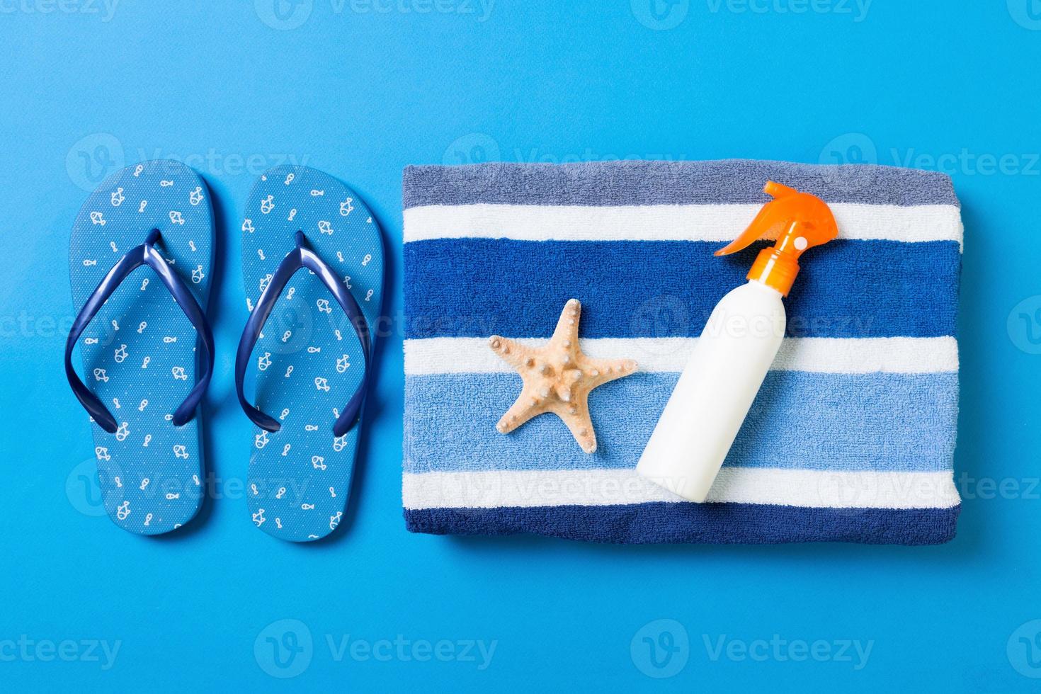 Top view of Beach flat lay accessories. sunscreen bottle with seashells, starfish, towel and flip-flop on Colored background with copy space photo