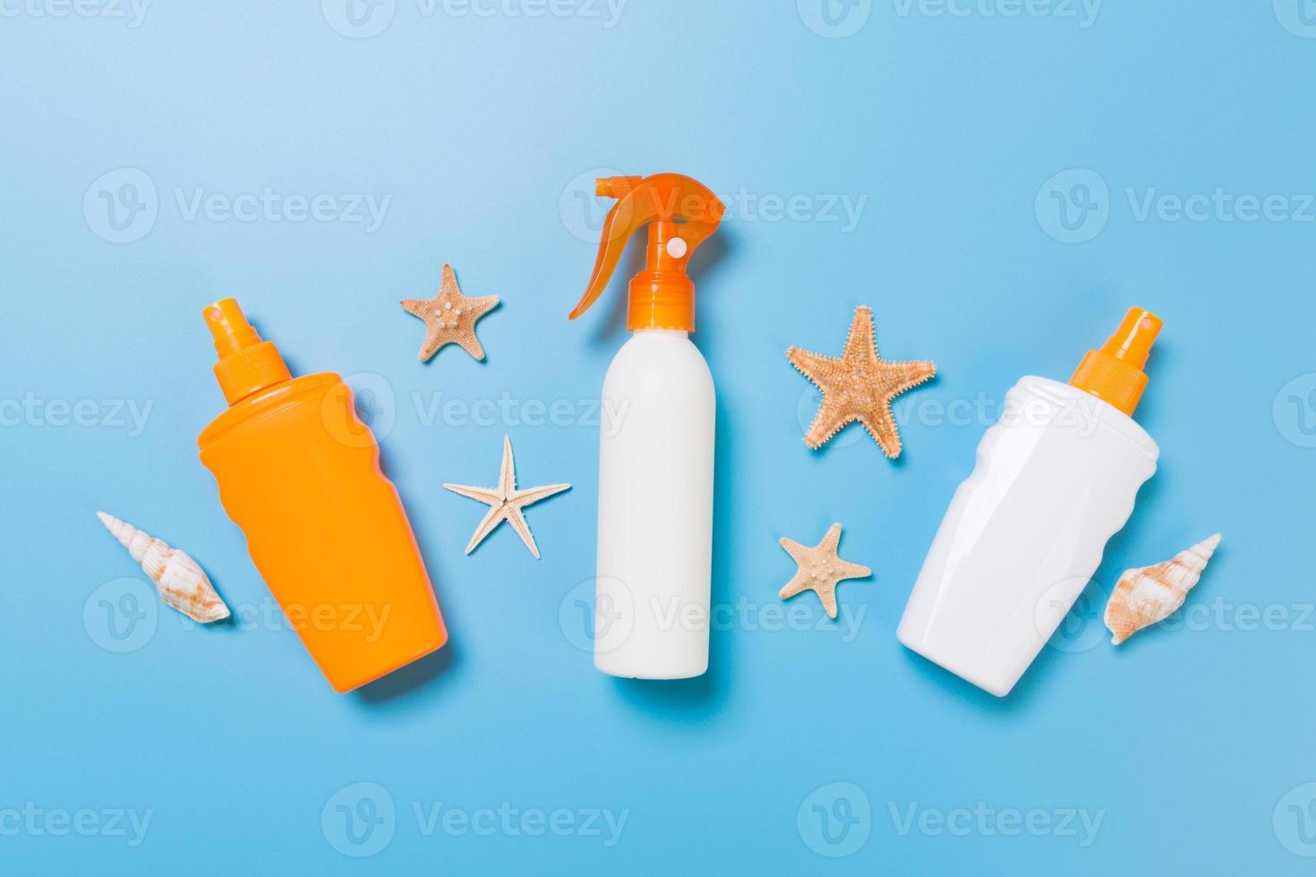 sunscreen cream with starfish and seashells in bottles on blue background, top view photo