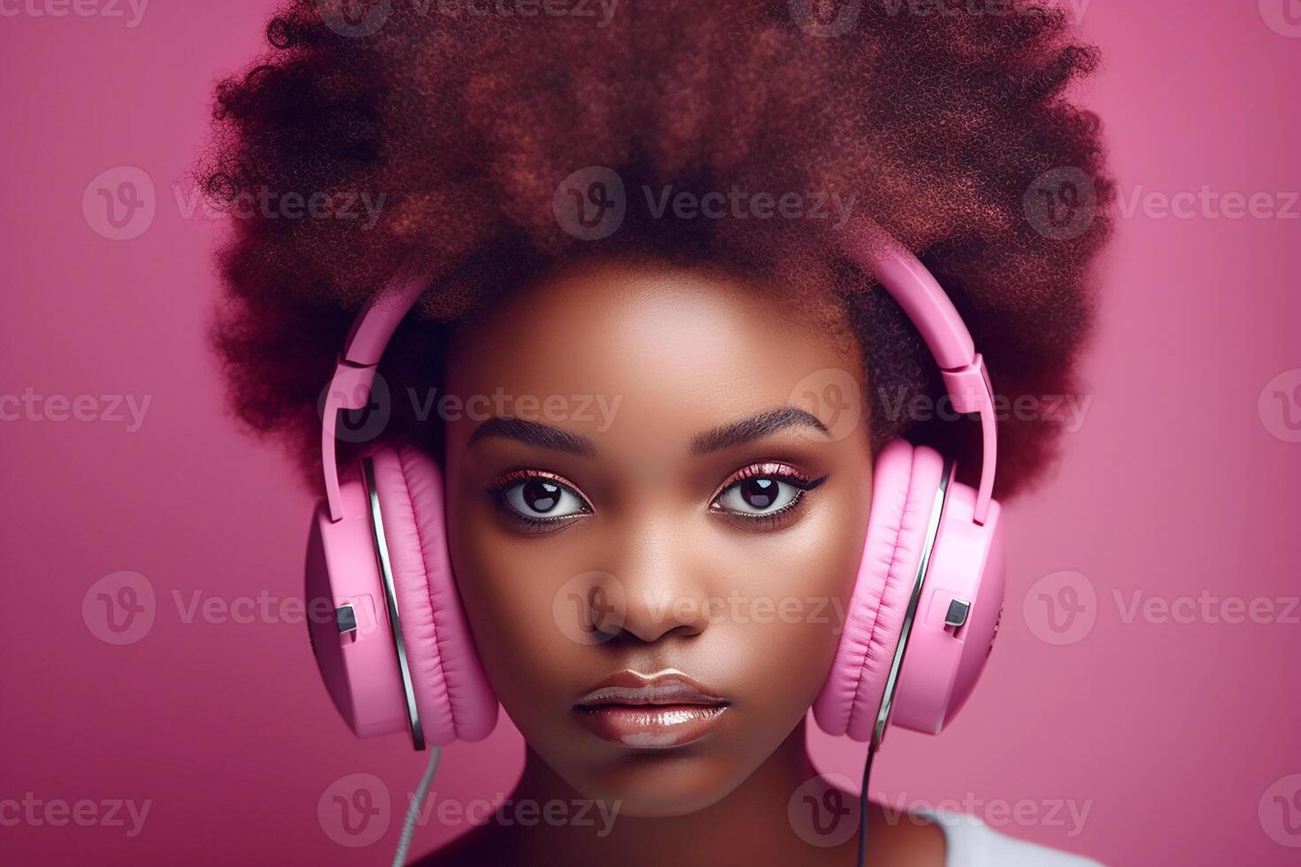 Dark-skinned African girl with black curly hair, wearing pink headphones on a pink background. Studio portrait. photo