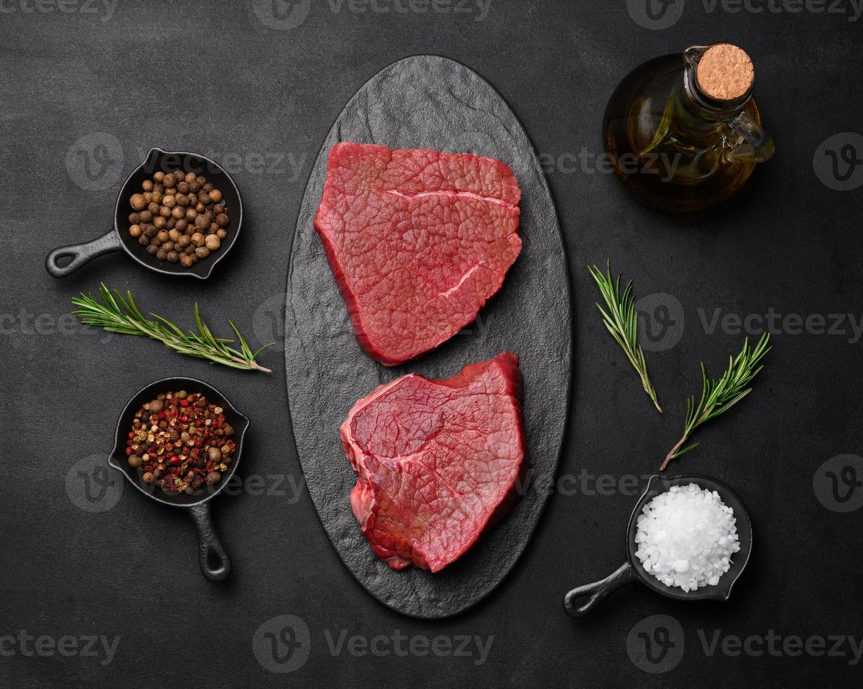 Raw piece of beef with spices pepper, rosemary sprig, salt and olive oil on a wooden board, black background. photo