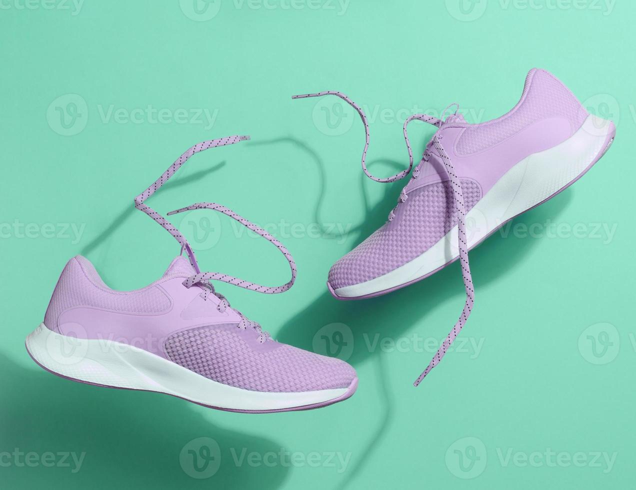 Purple women's sports sneakers with laces levitate on a green background. photo