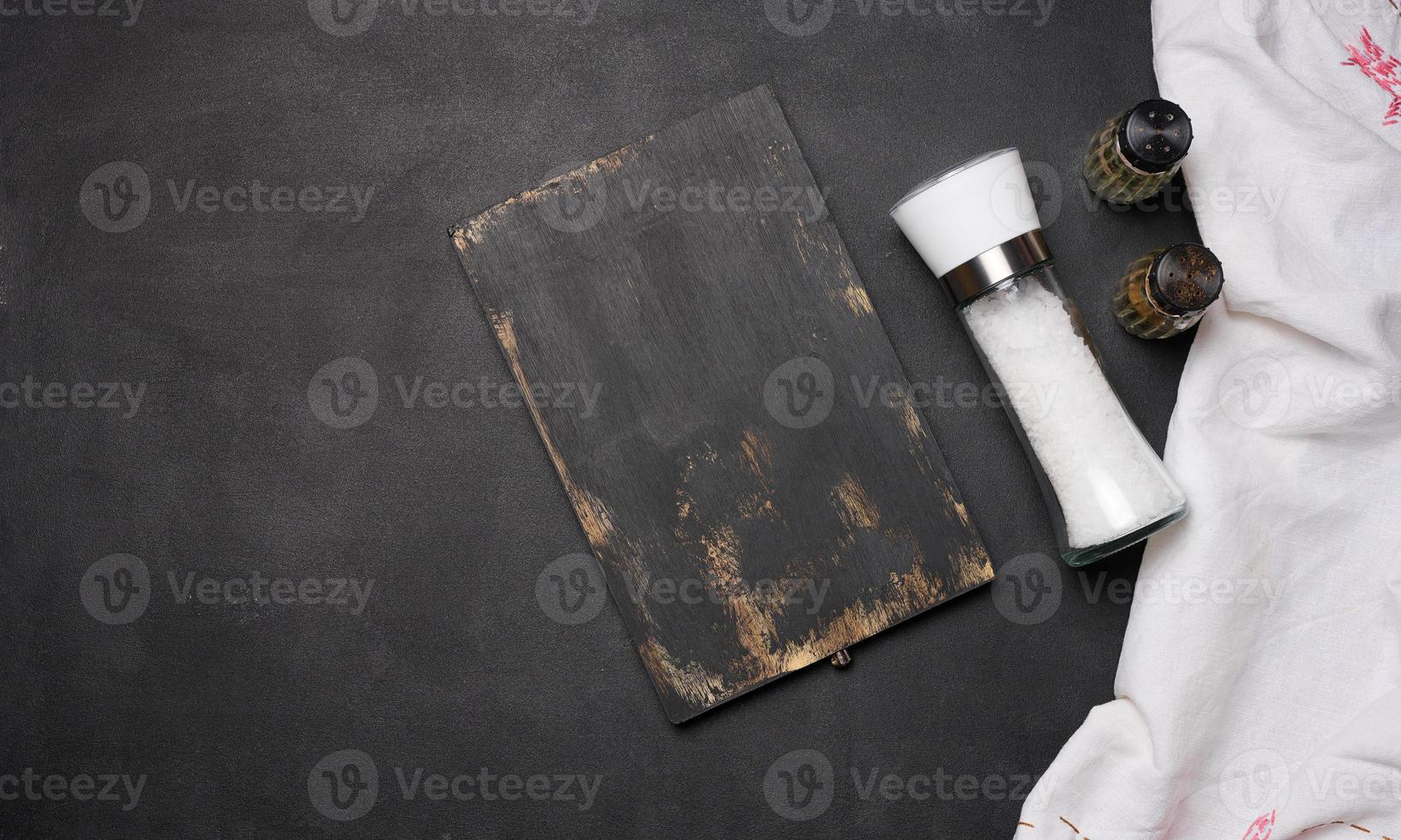 Empty black wooden board, salt in a glass bottle on a black table, top view photo