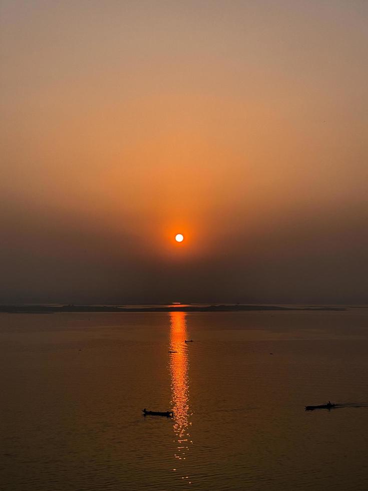 Sunset at the beach in the evening. A boat is going down the river with the sun setting behind it. photo