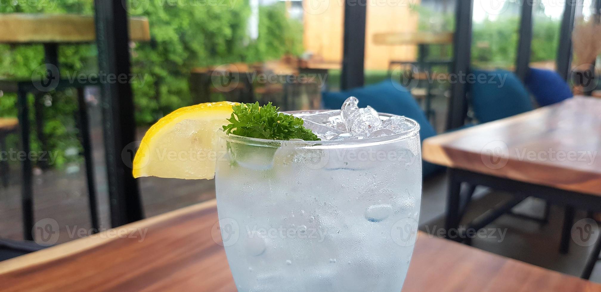 Close up fresh drinking cocktail with lemon slices and green herb leaves on top of glass with inside cafe shop background. Refreshment and Healthy life styl photo