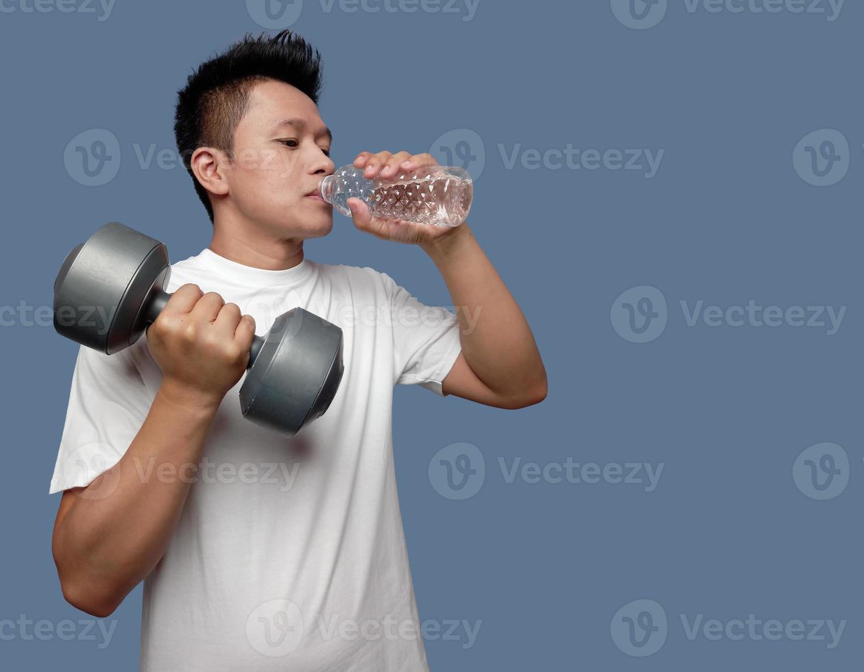 Young man is drinking while holding dumbbells isolated on plain background photo