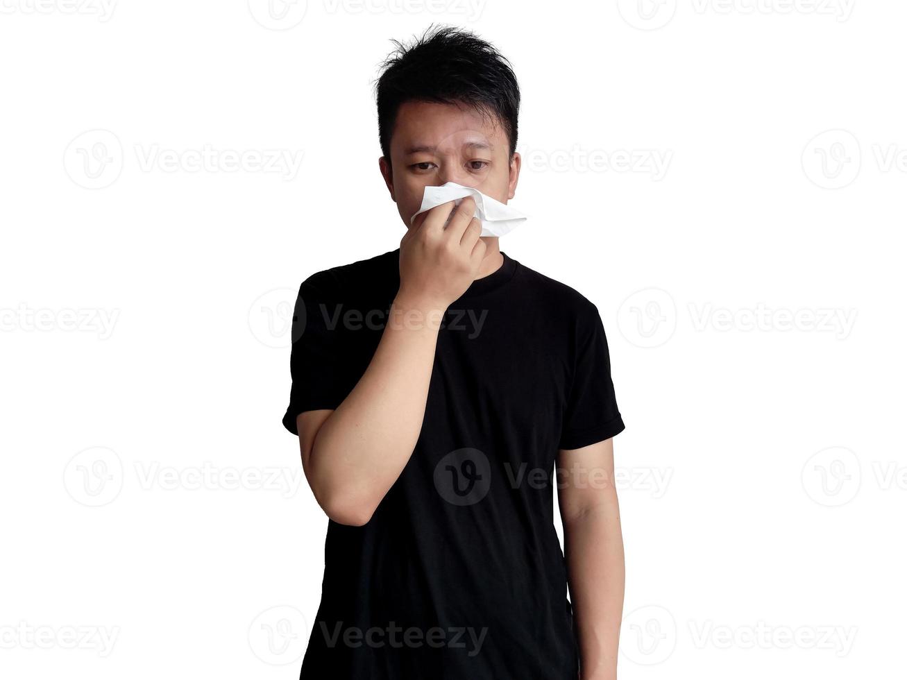 Young man in black shirt holding nose with tissue with straight face expression isolated on white background photo