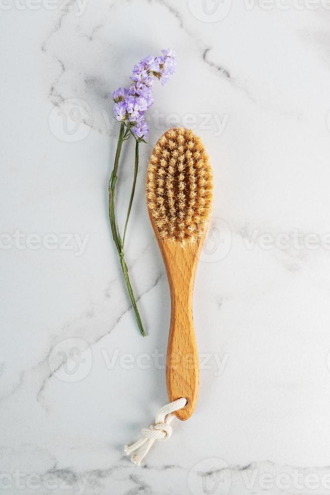 Dry massage brush made of natural materials on a light marble background. Beautiful flower nearby. Minimalism, copy space. photo