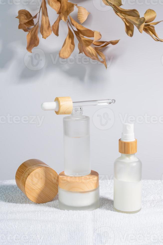 White frosted glass cosmetic bottles and jars with pamboo lids with tree leaves on white background. Skin care routine set for aging skin photo