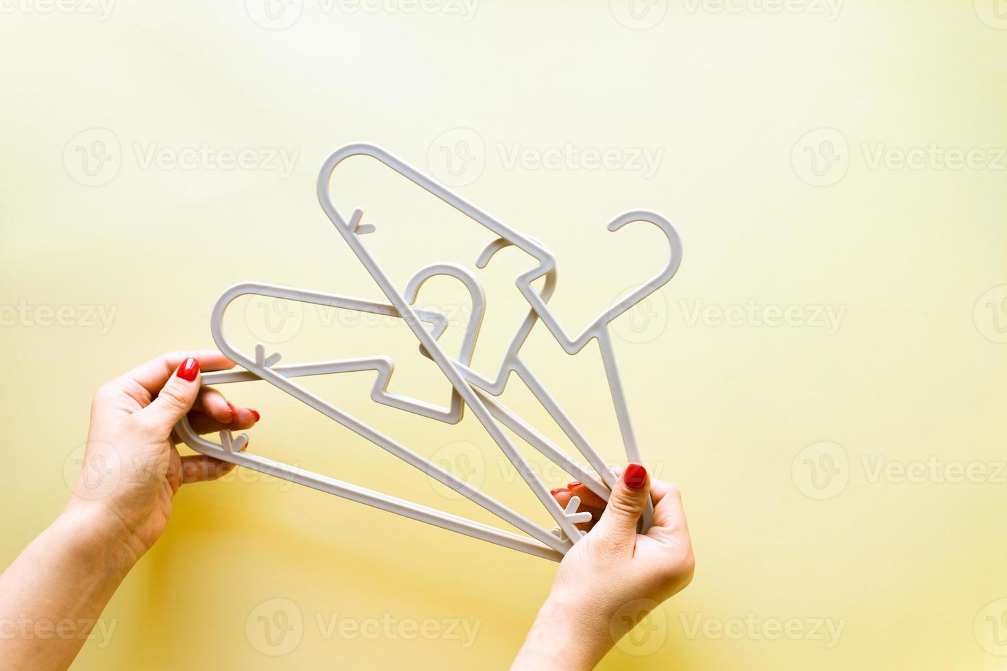 Hands holding baby hangers on yellow background photo