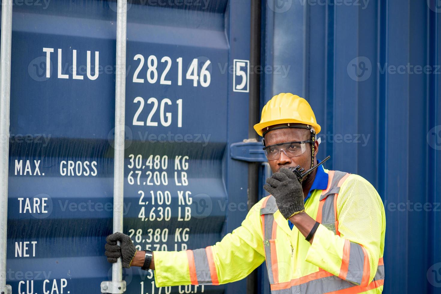 Worker man in protective safety jumpsuit uniform with yellow hardhat and use  Walkie Talkie check container at cargo shipping warehouse. transportation import,export logistic industrial service photo