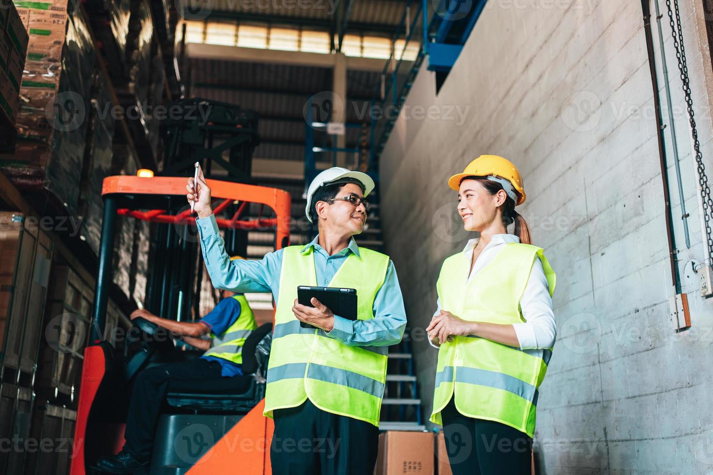 Working at warehouse. asian woman warehouse worker and Manager Shows Digital Tablet Information to further placement in storage department. In Background Stock of Parcels with Products photo