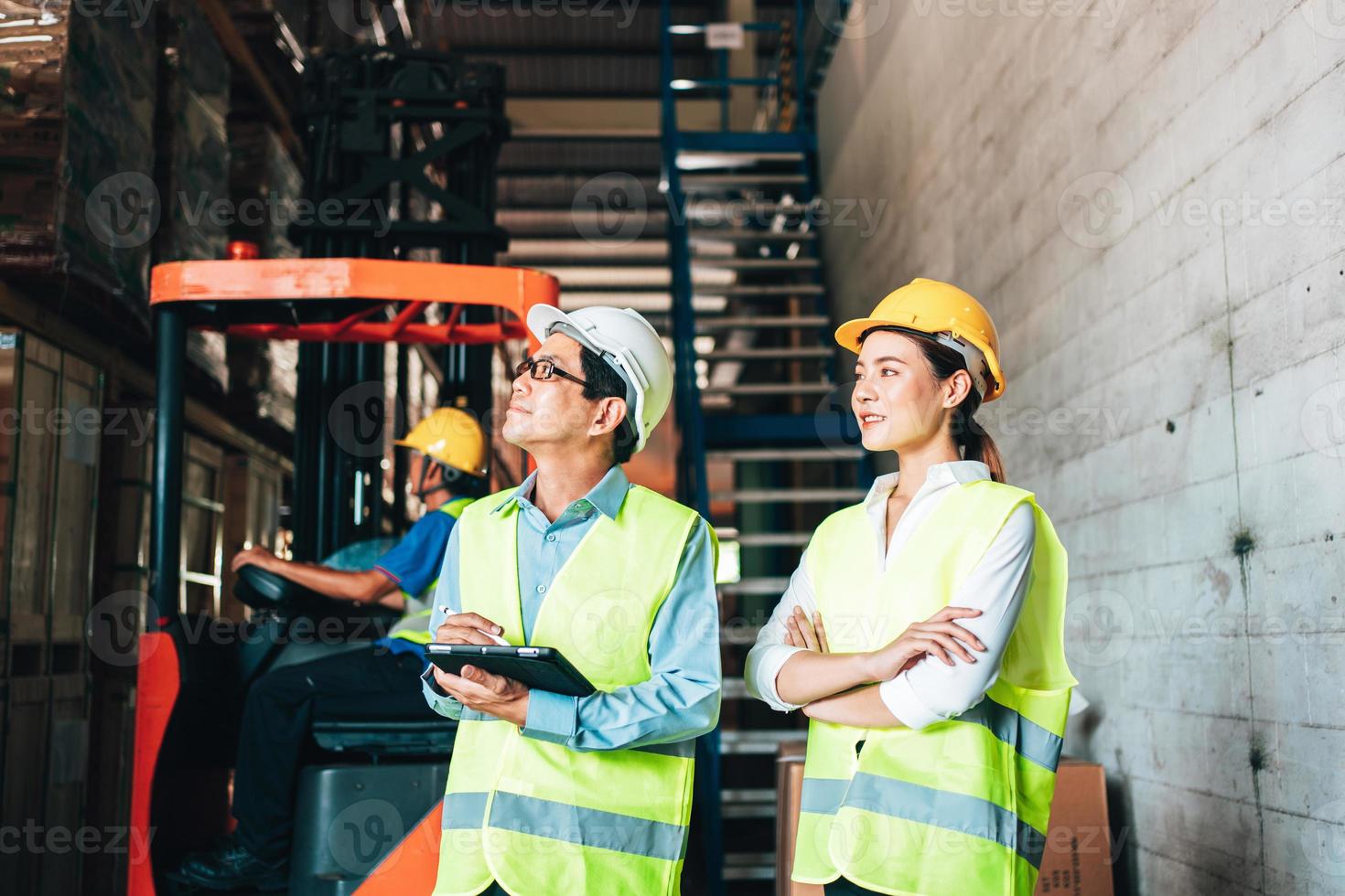Working at warehouse. asian woman warehouse worker and Manager Shows Digital Tablet Information to further placement in storage department. In Background Stock of Parcels with Products photo