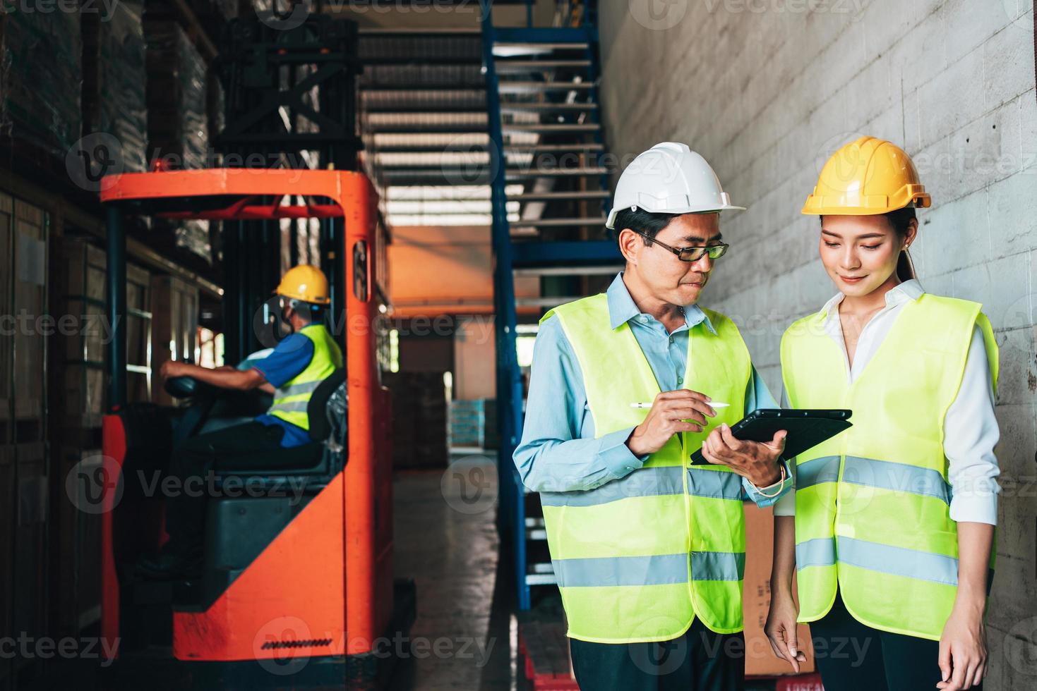 Working at warehouse. asian woman warehouse worker and Manager Shows Digital Tablet Information to further placement in storage department. In Background Stock of Parcels with Products photo