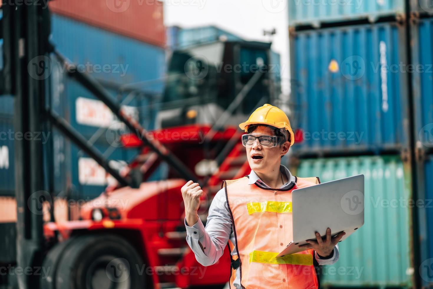 Asian technician dock worker in protective safety jumpsuit uniform and with hardhat and use laptop computer at cargo container shipping warehouse. transportation import,export logistic industrial photo