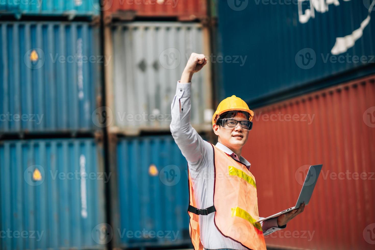 Asian technician dock worker in protective safety jumpsuit uniform and with hardhat and use laptop computer at cargo container shipping warehouse. transportation import,export logistic industrial photo