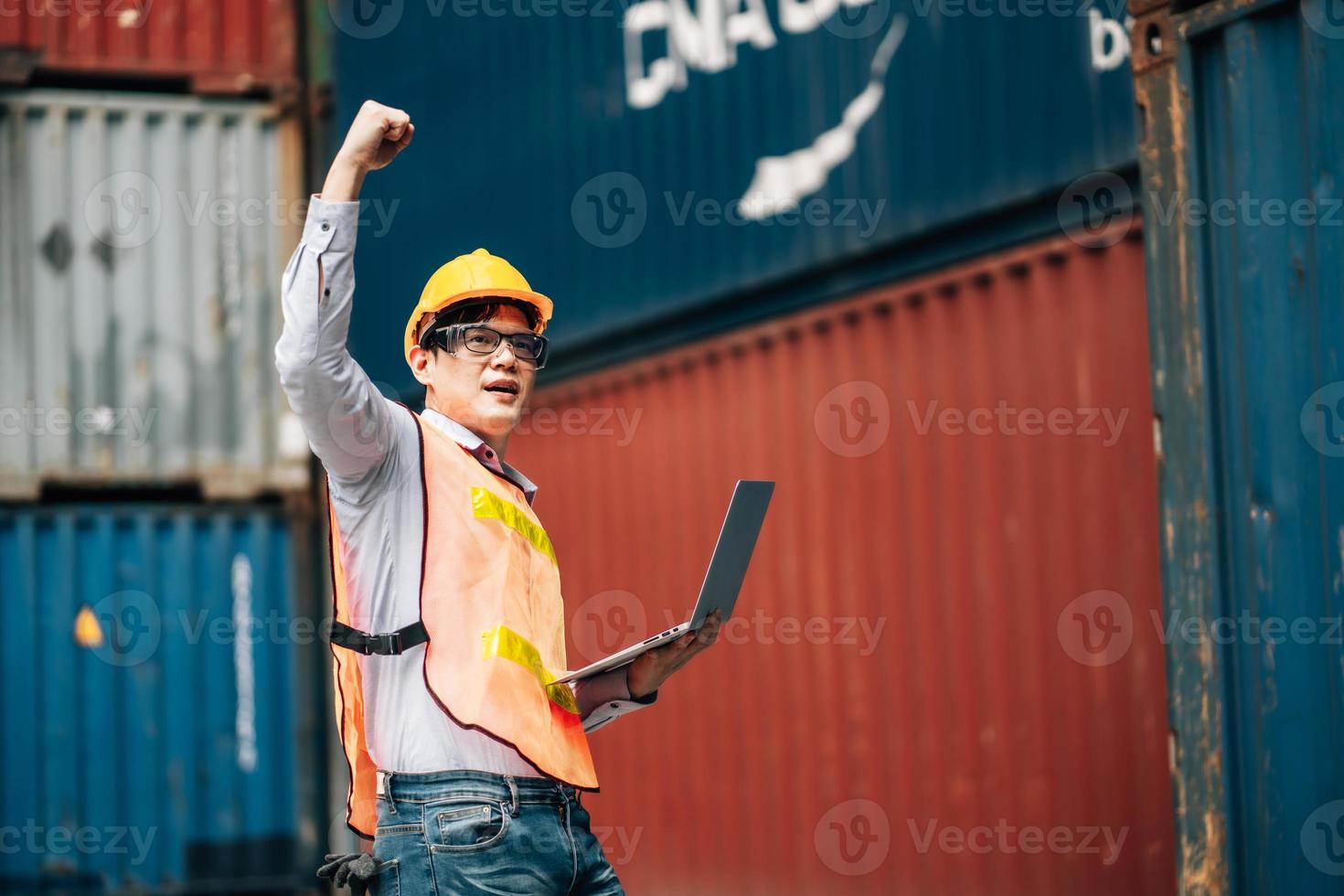 Asian technician dock worker in protective safety jumpsuit uniform and with hardhat and use laptop computer at cargo container shipping warehouse. transportation import,export logistic industrial photo