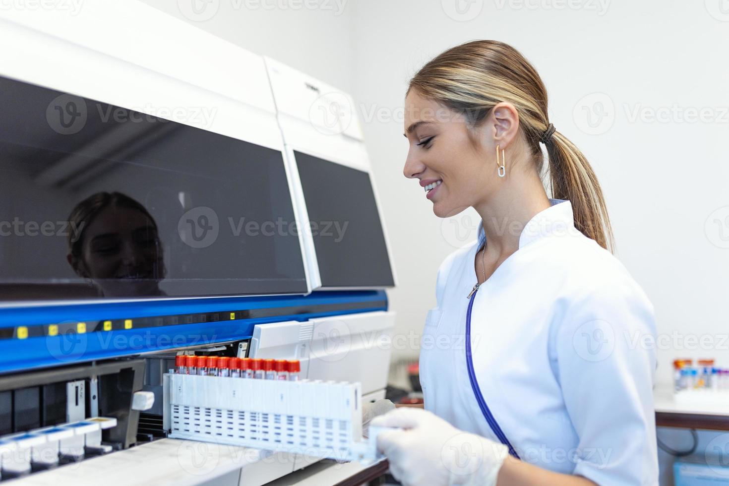 Lab tech loading samples into a chemistry analyzer. female lab tech loading specimen for coagulation test analysis photo