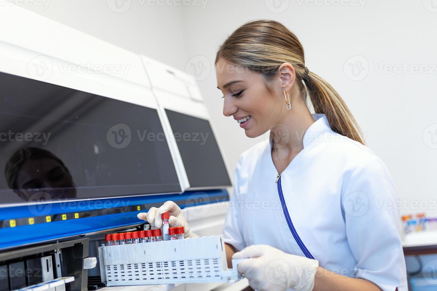 Portrait of a young female laboratory assistant making analysis with test tubes and analyzer machines sitting at the modern laboratory photo