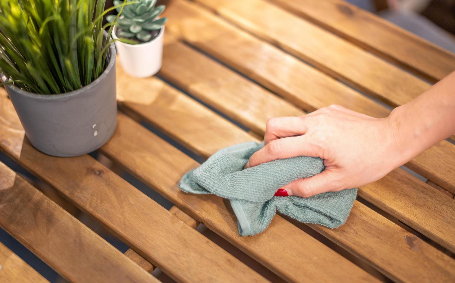 Close up female hand cleaning wooden table using disinfectant green towel. Prevent infection of Covid-19 virus, contamination of germs or bacteria, wipe or cleaning to eliminate. photo