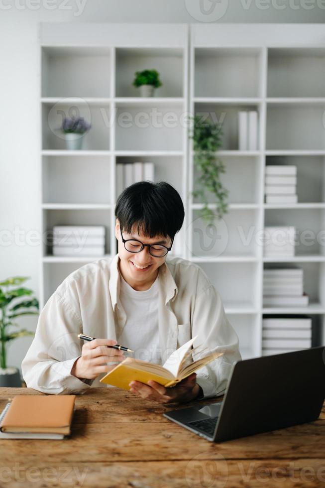 Handsome and talented young Asian man student working on his project assignment, using laptop and tablet to search an online informations. photo