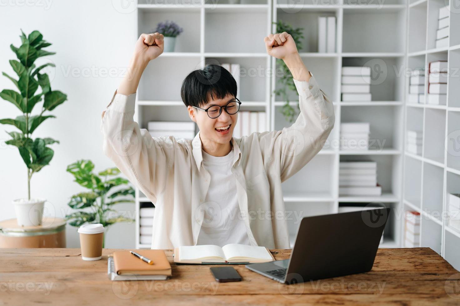 masculino estudiante tomando notas desde un libro a biblioteca, joven asiático sentado a escritorio haciendo asignaciones en Universidad biblioteca foto