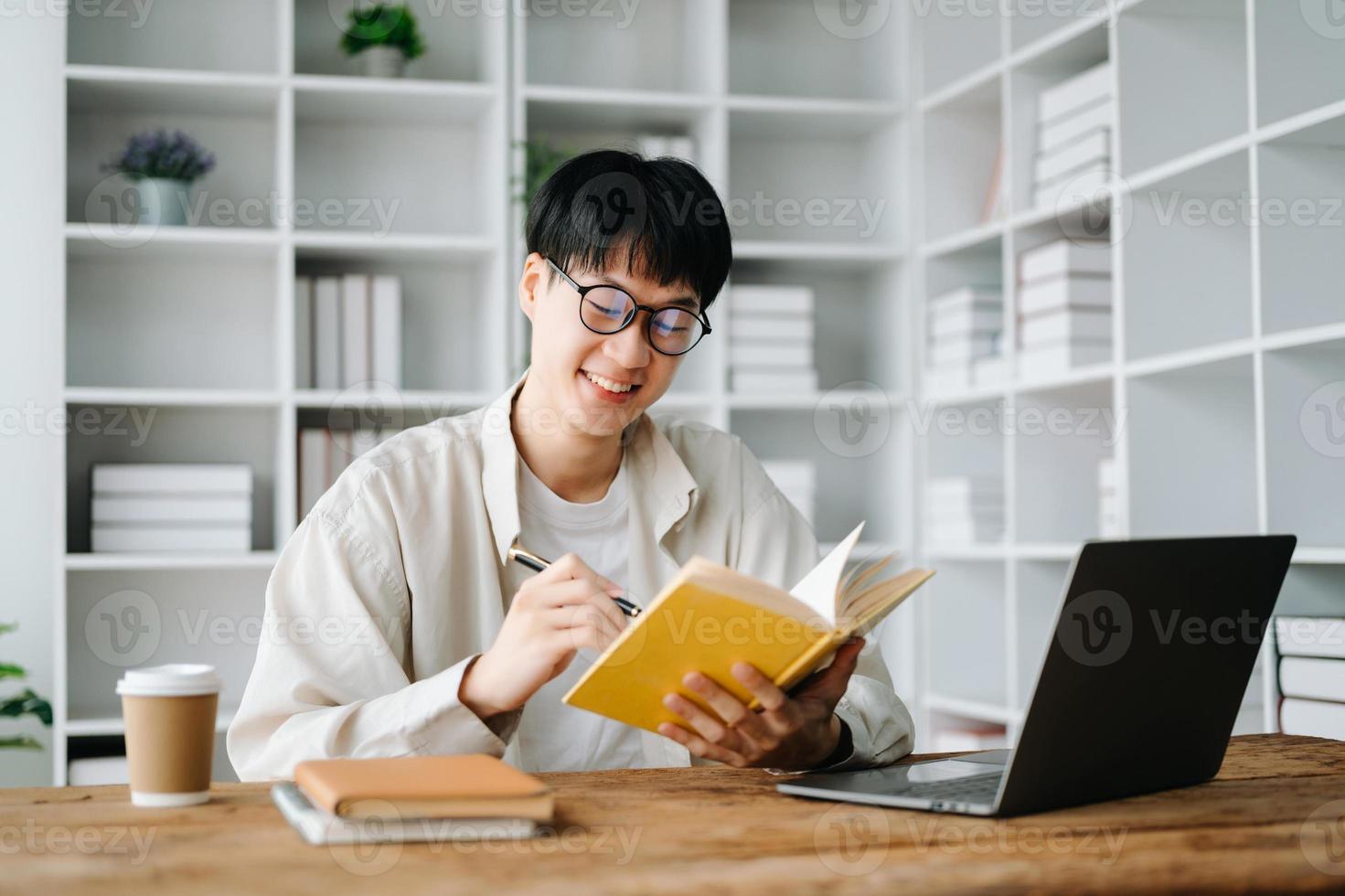 hermoso y talentoso joven asiático hombre estudiante trabajando en su proyecto asignación, utilizando ordenador portátil y tableta a buscar un en línea informaciones foto