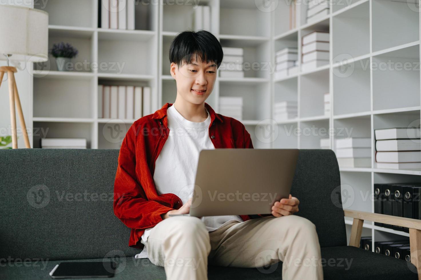 joven atractivo asiático hombre sonriente pensando planificación escritura en computadora portátil, tableta y ordenador portátil trabajando desde hogar a hogar oficina foto